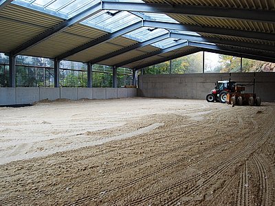 Reithallenbau in der Endphase, Traktor mit Planiergerät richtet die Tretschicht für gleichmäßige Reitbedingungen her