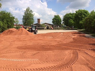 Einbau von rotem Reitplatzsand mit Traktor auf einem großen Reitplatz