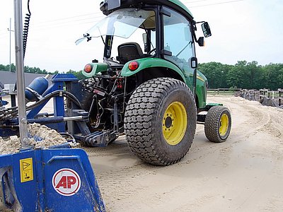 Traktor mit Planiergerät beim Verteilen von Reitplatzsand