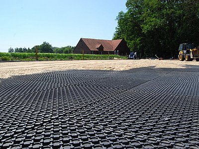 Verlegung von Kunststoffmatten auf dem Untergrund des Außenreitplatzes mit Radlader im Hintergrund