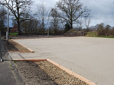Reitplatzfläche mit Randbegrenzung und Drainage, umgeben von Bäumen auf einer Außenanlage